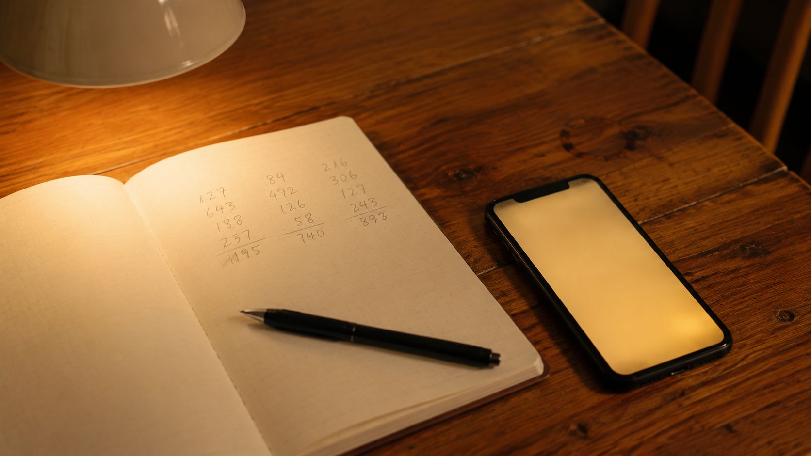 Notitieblok met een handgeschreven berekening van maandlasten naast een telefoon op een keukentafel